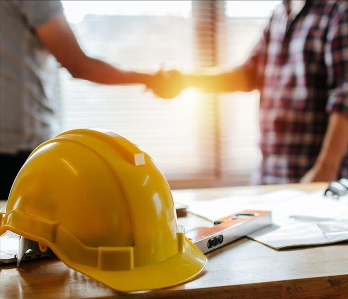 yellow safety helmet on workplace desk with construction worker team hands shaking